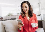 Younger woman looking at cell phone holding cup of coffee